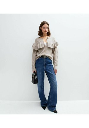 Beige knit cardigan with ruffled accents, gold buttons, paired with high-waisted, wide-leg blue denim jeans and a small black handbag.