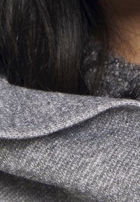 Tessuto grigio con una trama melangiata, dotato di colletto piegato e finitura liscia. Lo sfondo suggerisce capelli scuri.