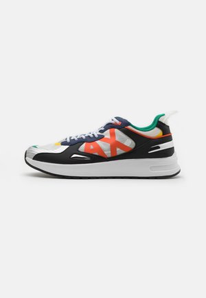 Sidet view af en hvid og sort sneaker med stort orange "AX" logo, grøn inderforing og hvide snørebånd på en ren hvid baggrund.