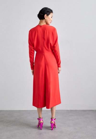 Vestido midi rojo con mangas largas, textura suave y un cierre sencillo en la espalda. Combinado con sandalias de tacón alto de color rosa brillante.