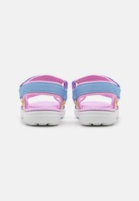 Sandalias infantiles con correas moradas y azules, interior rosa suave, suelas blancas y acentos amarillos. Diseño de espalda abierta para ventilación.