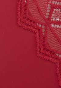 Tissu rouge ornée de détails en dentelle complexes dans un motif géométrique le long d'un bord, alliant des éléments lisses et texturés.