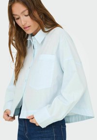 Light blue cropped button-up shirt in lightweight fabric, featuring a pointed collar, single chest pocket, and long sleeves.