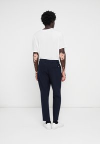 Pantaloni bleumarin cu o croială slim și buzunare laterale, asortați cu un tricou alb cu mânecă scurtă și adidași albi, văzuți din spate.