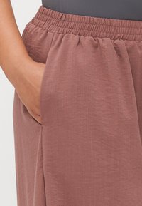 Rosa, lett stoff med en avslappet passform. Har elastisk midjebånd og sidelommer. Glatt tekstur med et naturlig stoffutseende.