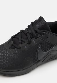Zapatilla deportiva negra de Nike con un patrón hexagonal texturizado, diseño elegante, material duradero y acentos brillantes contrastantes en los laterales.