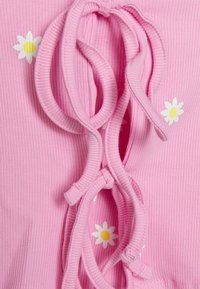 Tissu côtelé rose avec un détail à lacets et des marguerites blanches aux centres jaunes imprimées dessus.