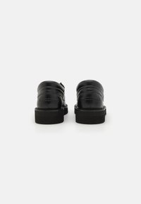 Zapatos de cuero negro con un acabado suave, punta redondeada y talón trasero acolchado. Cuentan con una suela de goma negra gruesa y detalles de costura mínimos.