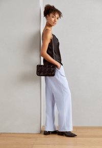 Czarna satynowa koszulka na ramiączkach zestawiona z jasnoniebieskimi spodniami o szerokich nogawkach oraz pikowaną czarną torebką na srebrnym łańcuszku. Prosty krój i smukła sylwetka.