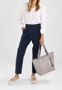 Lekka biała bluzka, granatowe spodnie z wysokim stanem, szara torba typu tote o gładkiej fakturze oraz beżowe mokasyny z detalem frędzli.