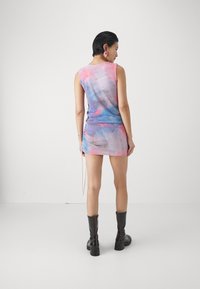 Dopasované bezrukávové šaty s ružovo-modrým vzorom tie-dye, s doplnkom na šnúrku, skombinované s čiernymi koženými čižmami po kolená.