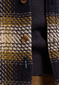Gebreide cardigan met een meerkleurig geometrisch patroon in marineblauw, crème en mosterd. Knopen in bruin. Label: Petrol Ind.
