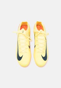 Žlté futbalové topánky Nike s čiernym logom swoosh, textúrovaným zvrškom a kontrastnou oranžovou podšívkou. Obsahujú štandardné šnúrky a zaoblenú špičku.