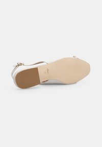 Sandal bianca con una tomaia liscia, sottile cinturino alla caviglia e suola piatta in gomma beige. Presenta un logo impressionato e una leggera trama sul cinturino.