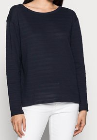 Marineblauwe longsleeve top met een gestreept textuurontwerp. Ronde halslijn en ontspannen pasvorm. Gemaakt in combinatie met witte broek, die eenvoudige details benadrukt.