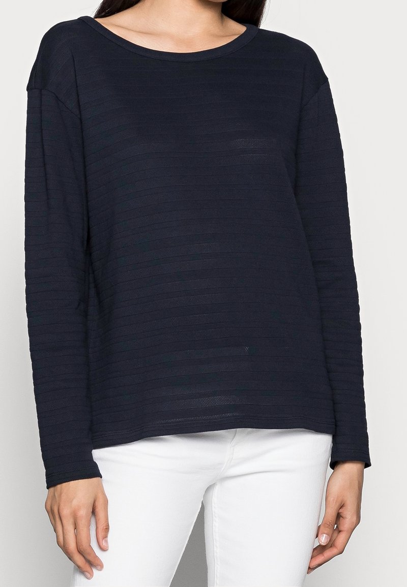 Marineblauwe longsleeve top met een gestreept textuurontwerp. Ronde halslijn en ontspannen pasvorm. Gemaakt in combinatie met witte broek, die eenvoudige details benadrukt.