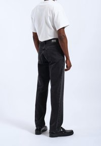 Vaqueros de denim negro con un corte relajado, que cuentan con bolsillos traseros y una cinturilla con marca. Llevados con una camiseta blanca y mocasines negros.