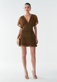 Brun, kort kjole med dyb V-udskæring og puffærmer, der har en tekstureret metallisk finish. Accentueret med guldtonede accessories.