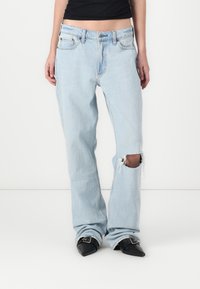 Light blue denim jeans with a relaxed fit, featuring a torn knee with frayed edges, and a high waist design. Styled with black pointed shoes.