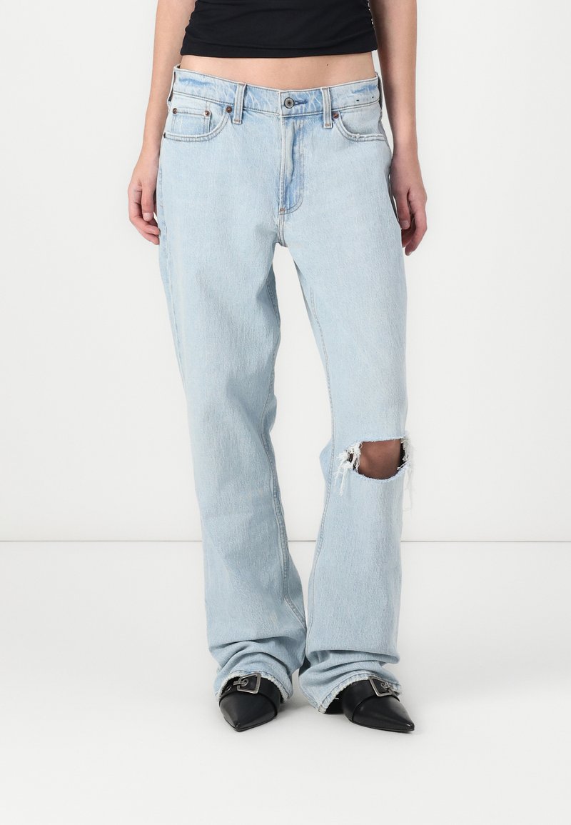 Light blue denim jeans with a relaxed fit, featuring a torn knee with frayed edges, and a high waist design. Styled with black pointed shoes.