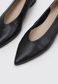Bailarinas de cuero negro con diseño de punta afilada, textura suave y tacón bajo. Forro interior en color neutro.