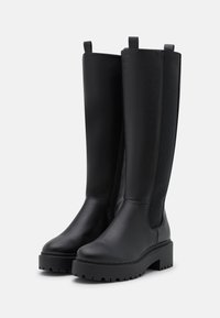 Schwarze knöchelhoche Stiefel aus glattem Leder mit einer klobigen Plateausohle. Verfügt über einen Reißverschluss an der Seite und einen flachen Absatz mit einer strukturierten Unterseite.