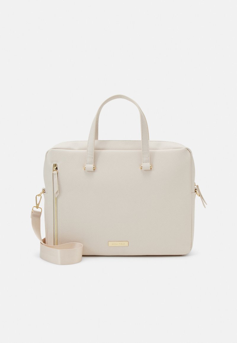 Sac à main synthétique beige avec double poignées, une bandoulière ajustable, des accents en métal doré, et un extérieur texturé avec une poche latérale zippée.