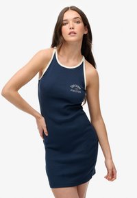Granatowa sukienka w prążki z kremowymi wykończeniami i graficznym logo "Superdry Athletics" na klatce piersiowej. Dopasowany krój, bez rękawów, z okrągłym dekoltem.