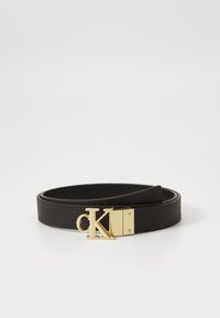 Cintura in pelle nera con finitura testurizzata, caratterizzata da una fibbia con logo "CK" dorato e una fodera interna liscia. Design semplice, forma arrotolata.