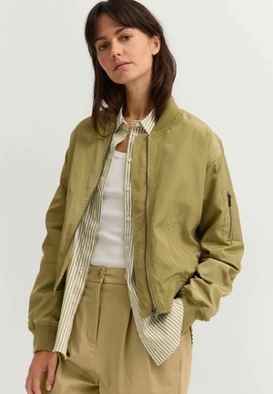 Olive green bomber jacket with a zip front, ribbed cuffs, and a side pocket. Paired with a white tank under a striped button-up shirt.