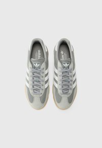 Grijze sneakers van mesh en suede, met witte strepen, grijze veters en een rubberen gumzool. Ontworpen voor comfort en ondersteuning.