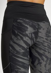 Czarne legginsy z wysokim stanem z teksturowanym szarym wzorem w paski tygrysa, z logo DryCell i gładkim, elastycznym materiałem.