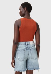 Roodbruine geribbelde tanktop gecombineerd met lichtblauwe versleten denim shorts, met gefragmenteerde zoom en een leren label op de tailleband.