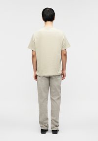 Ανοιχτό μπεζ βαμβακερό μπλουζάκι με χαλαρή εφαρμογή, συνδυασμένο με ανοιχτό γκρι φαρδιά παντελόνια, με θέα από πίσω. Απλός σχεδιασμός, χωρίς ορατά γραφικά.