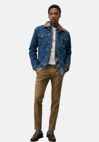 Giubbotto di jeans con colletto beige, t-shirt bianca e chinos marroni. Scarpe marroni scure con calzini a fantasia. Fit casual e design moderno.