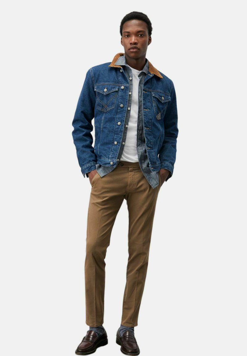 Giubbotto di jeans con colletto beige, t-shirt bianca e chinos marroni. Scarpe marroni scure con calzini a fantasia. Fit casual e design moderno.