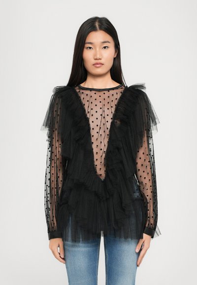 Black sheer blouse with polka dots, ruffled accents, and long sleeves; features a deep V-neck and fitted cuffs with textured fabric.
