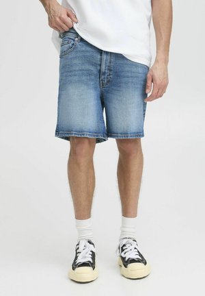 Lette blå denimshorts med lige snit og frynsede kanter. Kombineret med en hvid t-shirt og sorte sneakers.