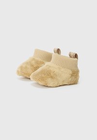 Tan fôrede støvletter med ribbet strikkekant og en liten stoffsløyfe bak for enkel påkledning. Myk tekstur og rund tådesign.