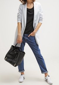 Jasnoszary żakiet, czarna bluzka, podwinięte niebieskie dżinsy, białe trampki, trzymająca czarną torebkę z fakturowanej skóry z złotymi akcentami.