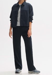 Granatowa kurtka z kołnierzem i guzikami, w parze z dopasowanymi spodniami o szerokich nogawkach. Pod spodem teksturowana szara bluzka. Buty sportowe, casualowy wygląd.