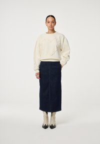 Ivoorkleurige sweatshirt met een gerimpeld hartontwerp, gecombineerd met een maxi-jurk van donker denim en crèmekleurige cowboystijl enkellaarsjes met zwarte accenten.
