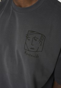 Mørk grå bomulds t-shirt med rund halsudskæring, prydet med en minimalistisk sort stregtegning af et ansigt og teksten "Resteröds" nedenfor.
