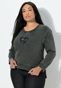 Sudadera gris oscuro con un diseño de corazón negro en el pecho, cuello redondo, mangas largas y aberturas laterales en el dobladillo. Textura suave.