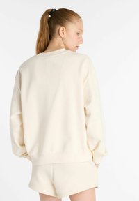 Sudadera de gran tamaño color crema, fabricada en tejido suave, con un escote redondeado y puños acanalados, acompañada de pantalones cortos a juego.