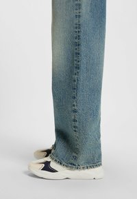 Cremfarbene Sportschuhe mit marineblauen Akzenten, kombiniert mit hellblauen Jeans aus Denim mit fransigem Saum und verwehter Textur.