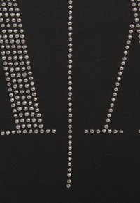 Svart tyg med silverfärgade dekorativa nitar arrangerade i geometriska mönster, som visar en strukturerad yta med framträdande, glänsande accenter.