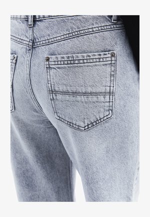 Jean en denim bleu clair avec un design classique à cinq poches, avec des coutures contrastées et une surface texturée. Poches arrière visibles.