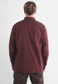 Chemise à manches longues bordeaux en coton avec une texture unie, poignets à boutons et un petit logo sur le haut du dos.