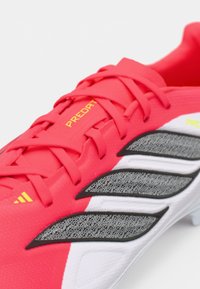 Φωτεινά ροζ ποδοσφαιρικά παπούτσια με υφή, που διαθέτουν μαύρες και άσπρες λεπτομέρειες και κίτρινη επωνυμία "PREDATOR" στο πλάι.